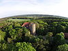 Eine Sicht von oben auf eine Burg umgeben von Wald und grüne Wiesen. Der Horizont wölbt sich leicht.