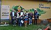 Eine Gruppe von Kindern und Erwachsenen haben sich für ein Gruppenfoto auf einer Wiese mit dem Kitagebäude im Hintergrund zusammengestellt.