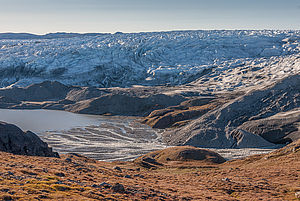 Hügelige Landschaft mit Eisbergen und Gletschern und einem See in der Mitte.
