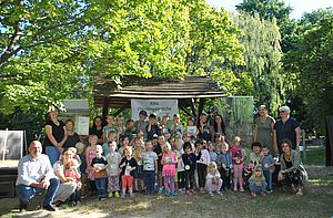 Eine Gruppe von Kindern und ein paar Erwachsenen haben sich für ein Gruppenfoto im Grünen zusammengestellt.